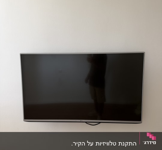 טלוויזיה מותקנת על קיר לבן עם השתקפות אדם